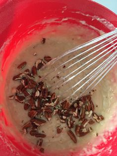 a red bowl filled with cream and pecans next to a whisk in it