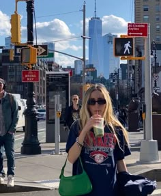 a woman drinking from a green cup while walking down the street in new york city