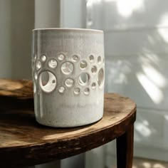 a white vase sitting on top of a wooden table next to a planter with holes in it