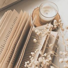 an open book next to a candle and some books on a table with dried flowers