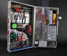 an open tool box filled with tools on top of a black table next to a wall