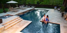 two women sitting on the edge of a swimming pool next to an outdoor hot tub