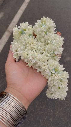 a person's hand holding some white flowers in their left hand on the street