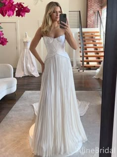 a woman in a white dress taking a selfie with her cell phone while wearing a wedding dress