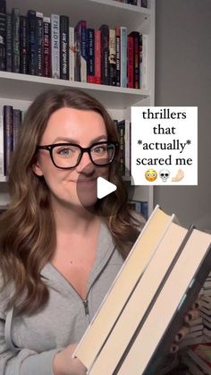 a woman holding a stack of books in front of a book shelf with an ad on it