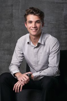 a young man sitting on top of a black chair wearing a white shirt and black pants