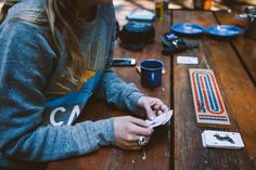 a woman sitting at a picnic table looking at her cell phone and other items on the table