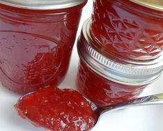 two jars filled with jam on top of a white surface next to a spoon full of jam