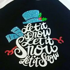 a black shirt with the words let it snow written in white and blue glitters