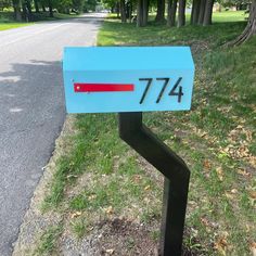 a blue mailbox sitting on the side of a road next to grass and trees