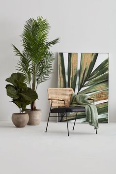 there is a chair next to a potted plant and a painting on the wall