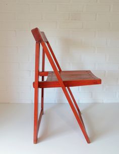 a red wooden chair sitting in front of a white brick wall on a white floor