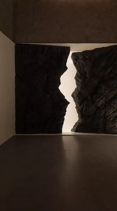 an empty room with two large rocks in the center and light coming from behind it