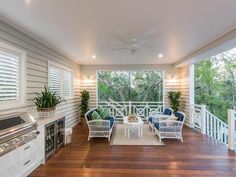 an outdoor kitchen and dining area with wood flooring, white walls and ceiling fans