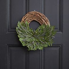 a wreath hanging on the front door of a house with green leaves and twigs around it