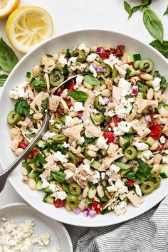 a white bowl filled with pasta salad next to sliced lemons and other ingredients on a table