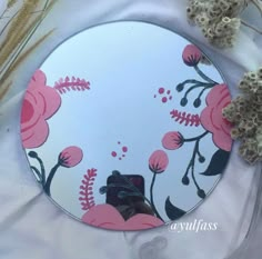 a mirror with flowers painted on it sitting next to some dried grass and dead plants