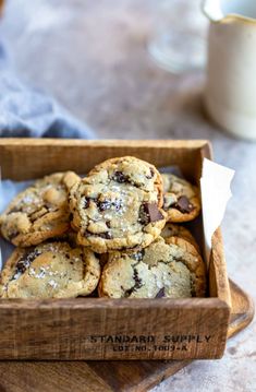 a wooden box filled with chocolate chip cookies on top of a table next to a glass of milk