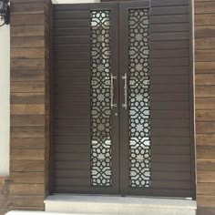 two brown doors with decorative glass on the side of a building in front of a white wall