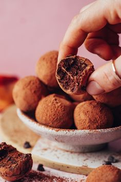 a person is picking up some chocolate truffles from a white bowl on a table