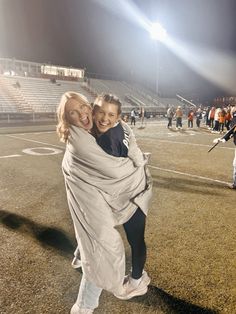 two women hugging each other on a field at night with fans in the stands behind them