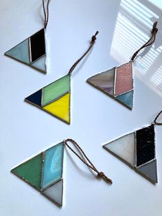 four pieces of stained glass hanging from strings on a white surface with sunlight coming through the window