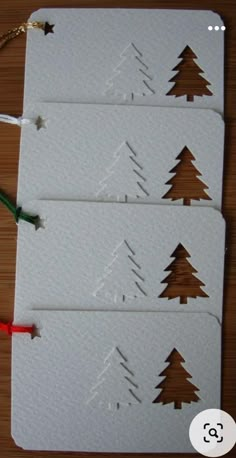 three white cards with brown trees cut out of them on a wooden table next to scissors and string