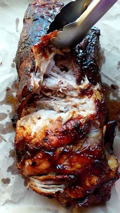 barbecue ribs with bbq sauce and tongs on top of them, sitting on wax paper