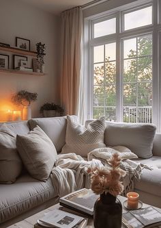 a living room filled with lots of furniture next to a window covered in blankets and pillows