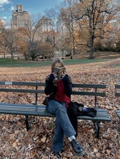 a woman is sitting on a bench in the park while holding up her cell phone