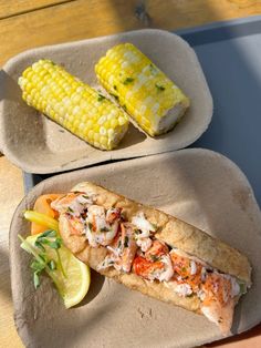 two plates with food on them sitting on a table next to corn and lemon wedges