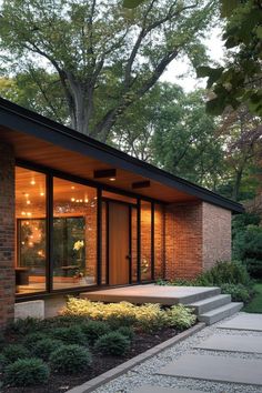 a small brick house with glass windows and steps leading up to the front door, surrounded by greenery