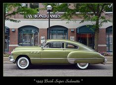 an old green car is parked in front of a brick building with a sign on it