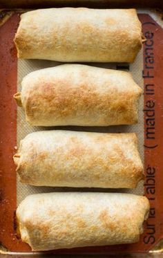 three burritos sitting on top of a baking pan covered in red chili sauce