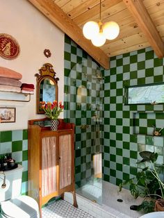 a green and white tiled bathroom with a wooden cabinet in the corner, potted plants on the counter