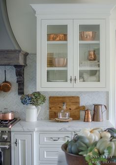 a kitchen with white cabinets and silverware on the counter top, next to a potted plant