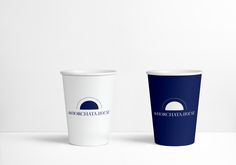 two paper cups sitting next to each other on a white counter top, with the same logo printed on them