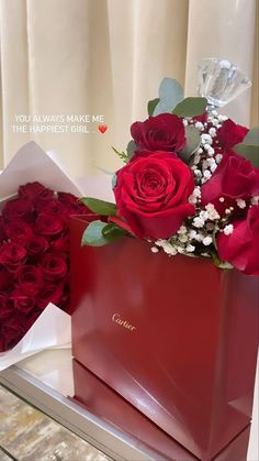 two red roses are sitting in a gift bag on a table with some other flowers