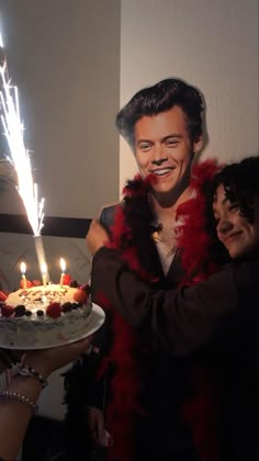 a man holding a birthday cake with lit candles on it while two women look on