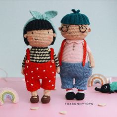 two crocheted dolls standing next to each other on top of a pink surface