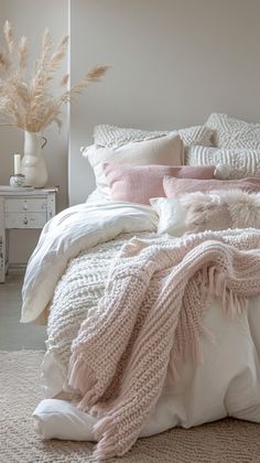 a white bed with pink pillows and blankets on top of it next to a dresser