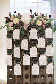 wine bottles are arranged on a wooden stand with tags attached to the top and flowers hanging from them