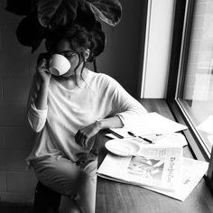 a woman sitting at a table drinking from a cup