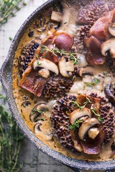 a pan filled with meat and mushrooms covered in mushroom gravy, garnished with fresh herbs