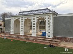 a small white gazebo sitting on top of a lush green field next to a building