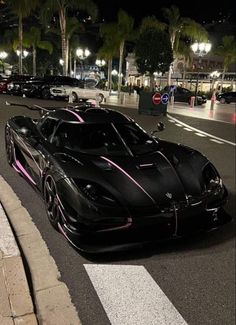 a black sports car with pink stripes on the hood driving down a street at night