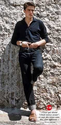 a man standing in front of a rock wall with his hands folded out and wearing sandals