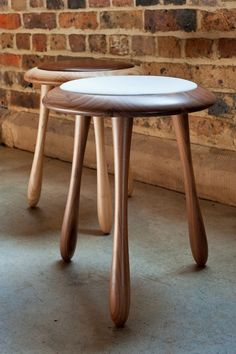 two wooden stools sitting next to each other in front of a brick wall and floor