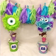 two cupcakes decorated with purple, green and blue tissue pom poms