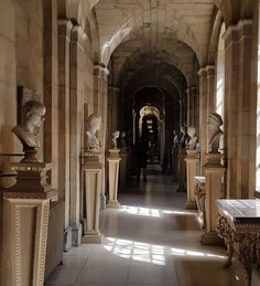 a long hallway with statues on either side and light coming in from the windows at the end